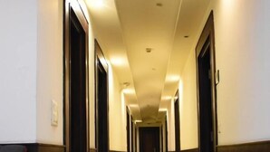 A long, narrow hotel corridor with doors on both sides, a central carpeted walkway, and recessed lighting. - Aaron Residency  (New Delhi)