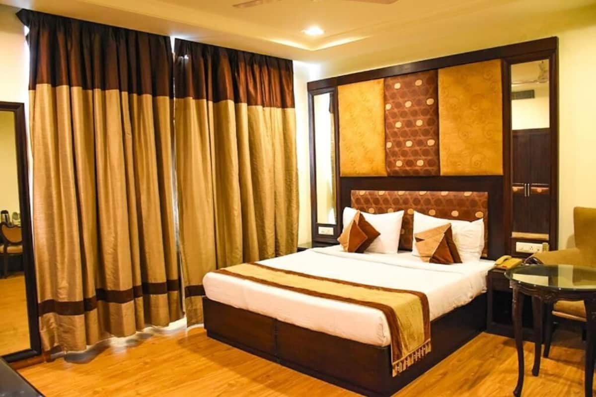 A hotel room with a large bed, a wooden headboard, a glass table, and a chair.