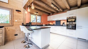 Eine moderne Küche mit Holzbalken, weißen Schränken und einer zentralen Kochinsel mit Barhocker.