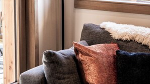 Ein gemütlicher Sitzbereich mit einer Couch und Kissen, einer Pendelleuchte und einem Fenster mit Blick auf eine Holzterrasse.