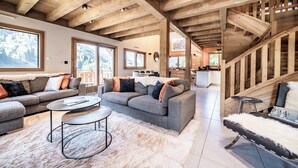 Ein großzügiger Wohnbereich mit hoher Holzbalkendecke, einer grauen Sofagarnitur, einem runden Couchtisch und einem flauschigen Teppich.
