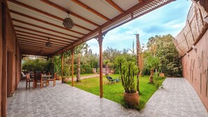 Een overdekt terras met betegelde vloer, houten meubels en potplanten.