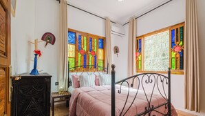 Een slaapkamer met een bed, een dressoir, een raam met glas-in-lood en een houten deur.