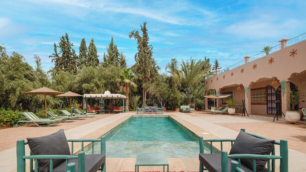 Un área junto a la piscina con sillones de descanso, una alberca y un edificio con arcos y barandilla.