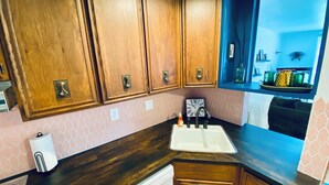 A kitchen with wooden cabinets, a sink, and a clock on the wall. - Color Me Crazy Eclectic Studio with Bay Views! (Daphne)
