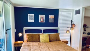 A bedroom with a large bed, a nightstand, a lamp, and wall art. - Color Me Crazy Eclectic Studio with Bay Views! (Daphne)