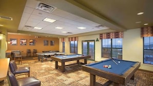 Una sala con mesas de billar, sillas y vistas a la ciudad.
