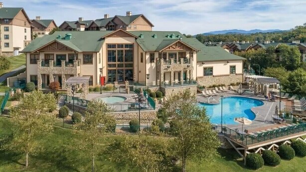Un resort con varias edificaciones, una piscina grande y un césped bien cuidado.