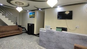 A reception area with a marble counter, a sofa, a staircase, and a TV on the wall. - Hotel O Taj Holiday  (Agra)