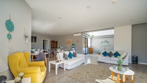 Een moderne woonkamer met een gele fauteuil, witte banken en een eethoek op de achtergrond.