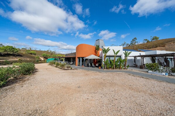 A modern building with a curved orange facade, a covered outdoor seating area, and a gravel driveway.