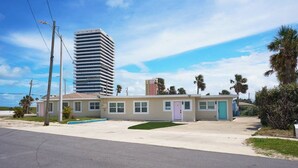 Ein eingeschossiges Motel mit einem kleinen Parkplatz, einem Pool und Blick auf ein hohes Gebäude im Hintergrund.