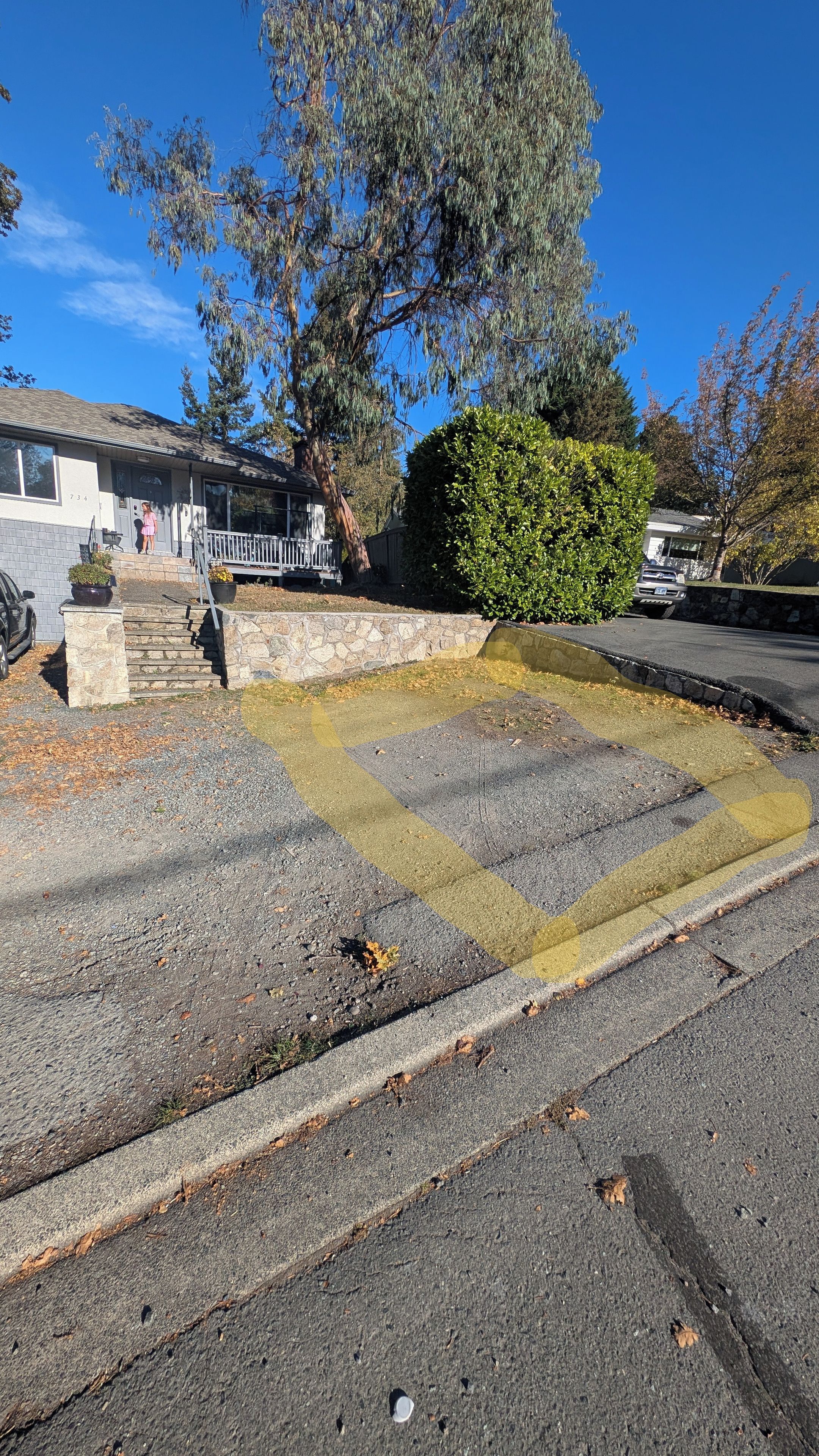Une allée menant à une résidence, avec un mur en pierre et un véhicule garé dans la rue.