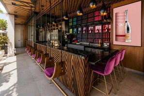 Uma área de bar com balcão de madeira, várias luminárias pendentes e um aparador de vinhos com garrafas.