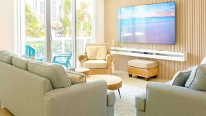A modern living room with a sofa, armchairs, a TV, and a balcony with outdoor furniture.