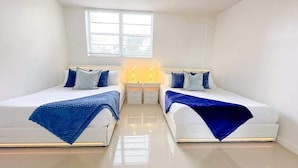 A bedroom with two beds, a nightstand, a window, and a light fixture.