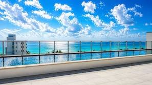 Piscina no terraço com vista clara para o oceano e um edifício ao fundo.