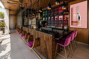 Uma área de bar com balcão de madeira, várias luminárias pendentes e um aparador de vinhos com garrafas.