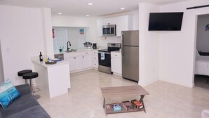 A modern apartment with a kitchen, dining area, and living room. It includes a flat-screen TV, a coffee machine, and a refrigerator.