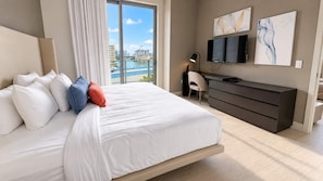 A hotel room with a large bed, a desk, a TV, and a view of a body of water.