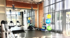 Uma academia com equipamentos de ginástica, amplas janelas e uma parede de tijolos.