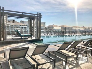 A rooftop pool area with sun loungers and a view of buildings in the background.