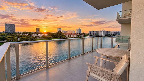A balcony with a view of a city skyline and a body of water at sunset.