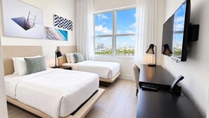 Quarto de hotel com duas camas, uma mesa de escritório com computador, televisão e vista para a cidade.