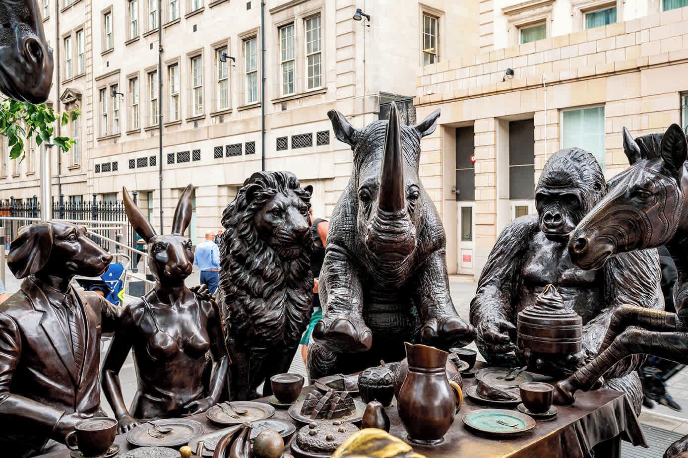 A sculpture of animals and humans at a table with food items.