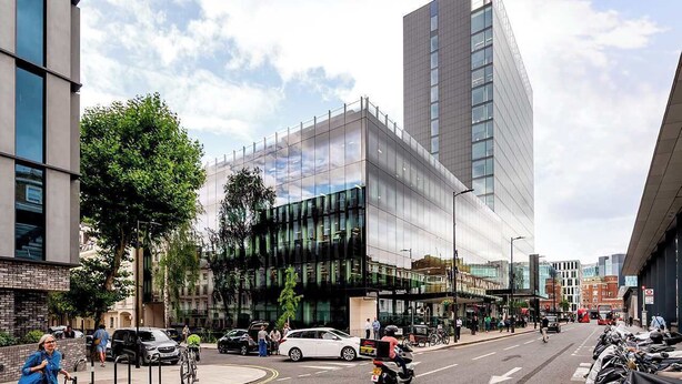 Un bâtiment moderne doté d’une façade en verre, d’une entrée d’angle remarquable et d’un espace de stationnement avec des supports à vélos.