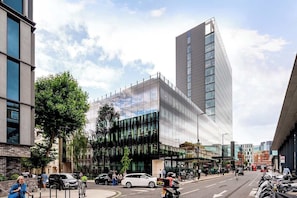A modern building with a glass facade, a prominent corner entrance, and a parking area with bicycles. - The Paddington Professional - by Out of Office Lifestyle (London)