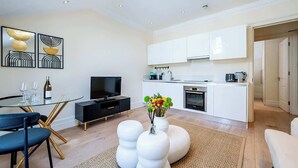Un salon moderne avec une table à manger en verre, un meuble de rangement pour appareils multimédias noir et un canapé blanc.