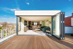 A modern apartment with a wooden deck, a living area with a sofa and coffee table, and a kitchen visible through glass doors. - Maison De Brompton With 1 Bedrooms and 1 Bathrooms (London)