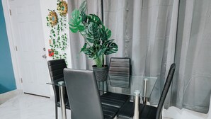 A dining area with a glass table and black chairs, a potted plant, and a fire alarm on the wall.