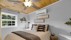 A bedroom with a bed, a ceiling fan, a window, and a wall-mounted air conditioner.