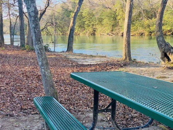 Una mesa de picnic verde en un parque, con árboles y un cuerpo de agua al fondo.