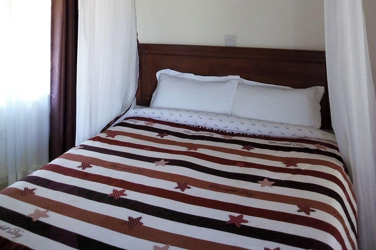 Un lit simple avec une couvre-lit à rayures, une table de chevet avec une lampe et une fenêtre avec des rideaux.