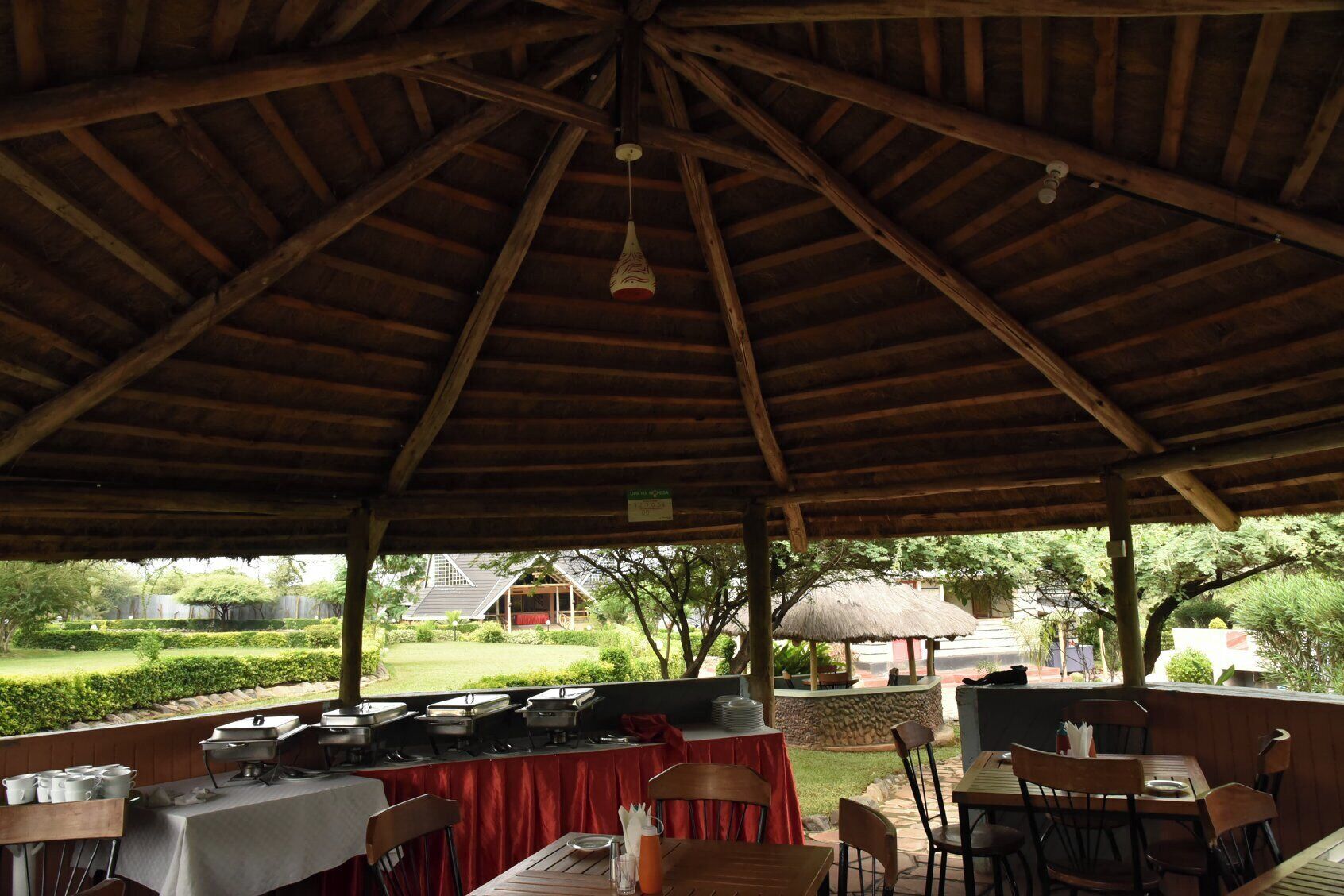 An outdoor dining area with a covered roof, tables set for meals, and a buffet setup.