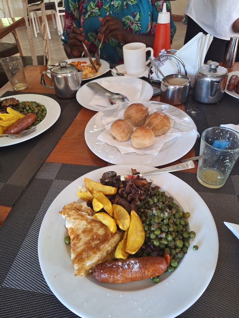 A dining table with plates of food, including sausages, peas, and potatoes.