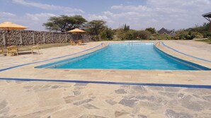 Una piscina rectangular con solarium de piedra, rodeada de mobiliario exterior y un muro de piedra.