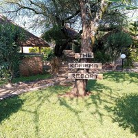Un cartel con la inscripción 'THE KORIEMA RESORT', rodeado de vegetación y una estructura con techo de paja.