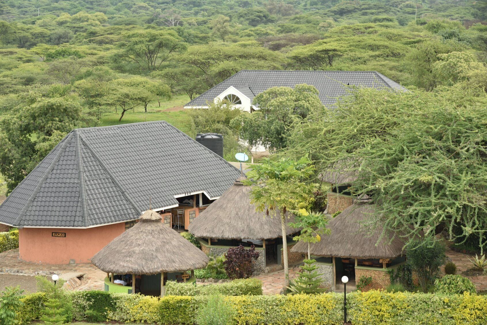 A lodge with thatched-roof huts and a main building with a tiled roof, surrounded by lush greenery.
