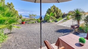 A patio with a table and chairs, surrounded by potted plants and a view of the ocean.