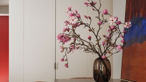 Un coin repas avec une table en bois et quatre chaises, un vase rempli de fleurs roses et un tableau accroché au mur.