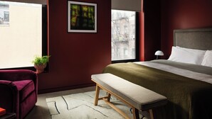 Une chambre moderne avec un grand lit, un banc, une plante en pot et un tableau abstrait encadré.