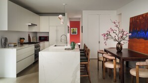 Une cuisine moderne avec des meubles blancs, un îlot en marbre et un coin repas comprenant des chaises en bois et une table en bois foncé.
