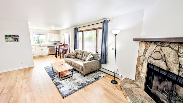 A modern living room with a stone fireplace, a sofa, a coffee table, and a dining area with a kitchen in the background. - Brand New Large 2Bd/1Ba Apartment - Near Downtown, King Bed! (Anchorage)