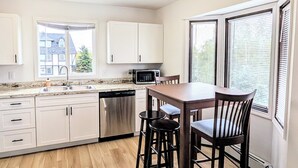 A modern kitchen with white cabinets, a wooden dining table, and bar stools. - Brand New Large 2Bd/1Ba Apartment - Near Downtown, King Bed! (Anchorage)