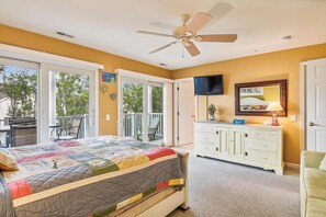 Un dormitorio con cama, cómoda, televisor y balcón.