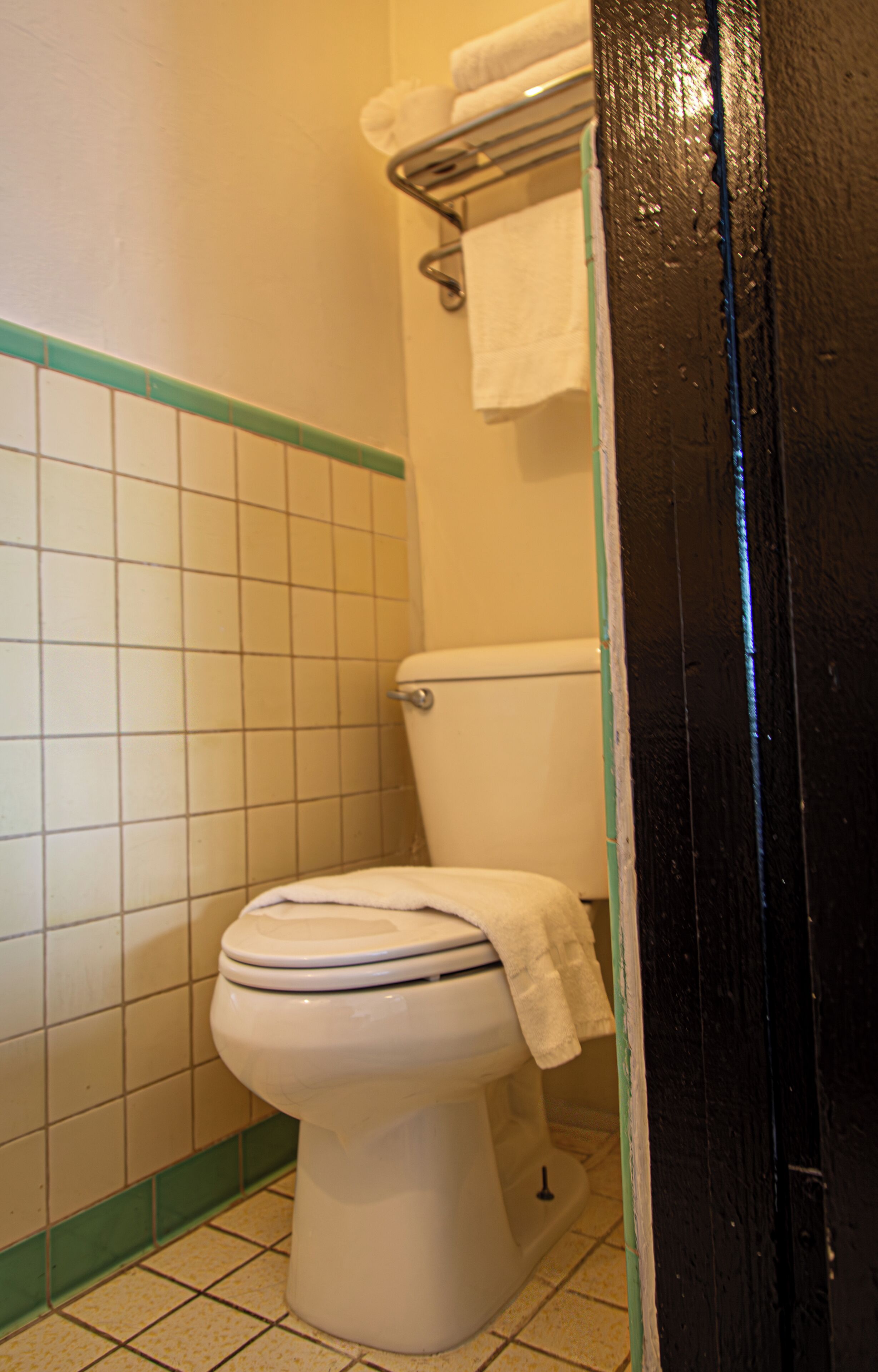 A toilet with a white seat and lid, a towel hanging on the wall, and a black door frame.